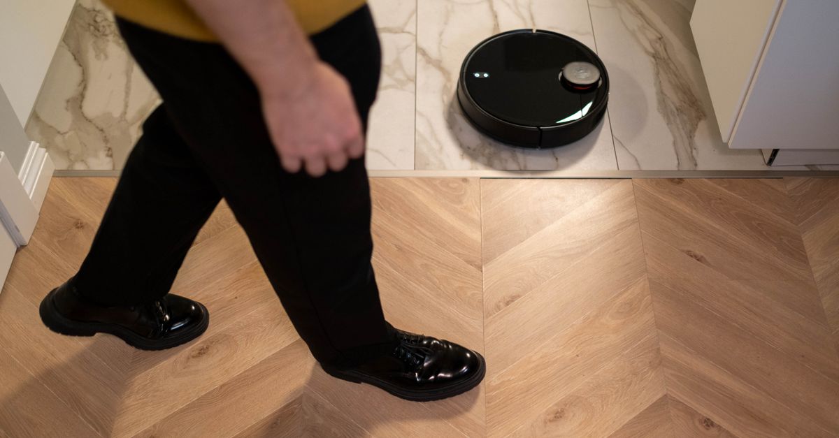 A robotic vacuum cleaner operating on a wooden floor, viewed in high angle indoor setting.