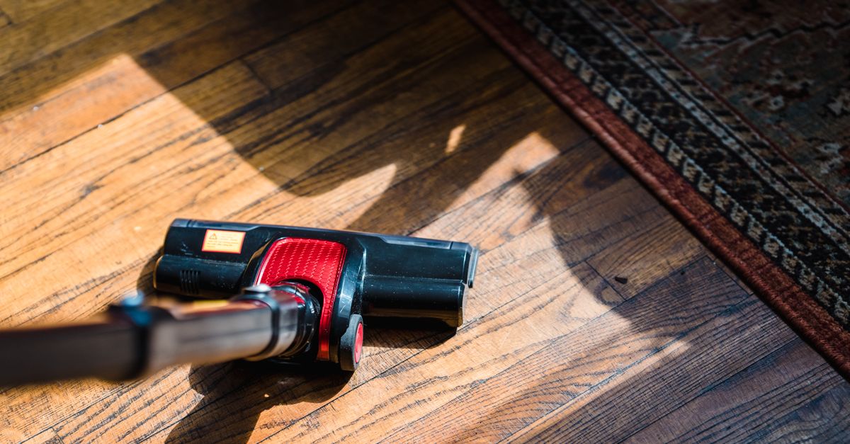 Close-up of a vacuum cleaner on wooden flooring near a patterned rug, showcasing domestic cleaning.